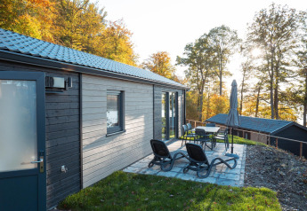 Außenterrasse mit Liegen und Esstisch an der Hackfort-Lodge, umgeben von herbstlichen Bäumen.