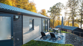 Patio with lounge chairs and dining set outside Hackfort lodge, surrounded by autumnal forest trees.