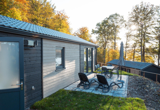 Terraza con tumbonas y mesa junto a la cabaña Hackfort, rodeada de árboles en colores otoñales.