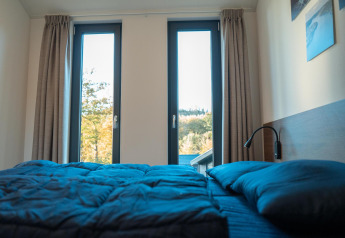 Schlafzimmer in der Hackfort Lodge am Biggesee, Deutschland, mit modernen Fenstern und blauer Bettwäsche.