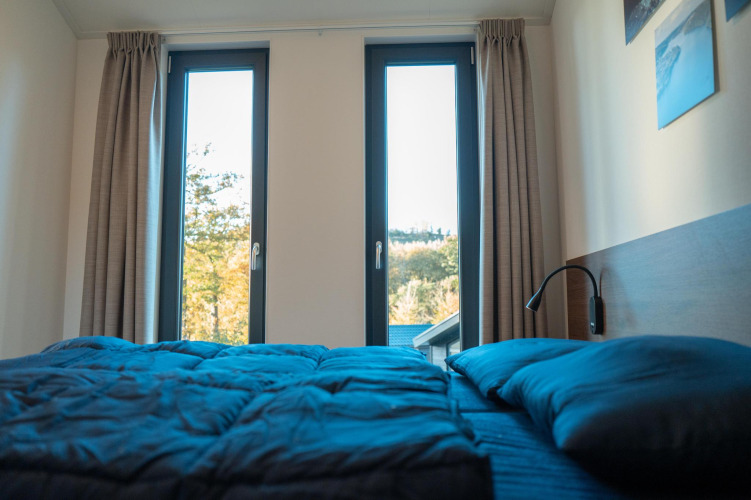 Dormitorio en Hackfort Lodge en Biggesee, Alemania, con ventanas modernas y ropa de cama azul.