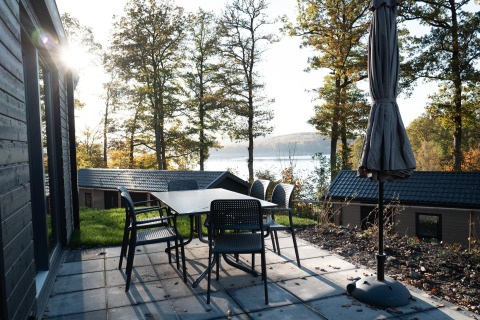 Terraza con mesa y sillas en el lodge Hackfort, con vista al lago y bosque en Biggesee, Alemania.