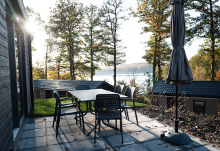Terraza con mesa y sillas en el lodge Hackfort, con vista al lago y bosque en Biggesee, Alemania.