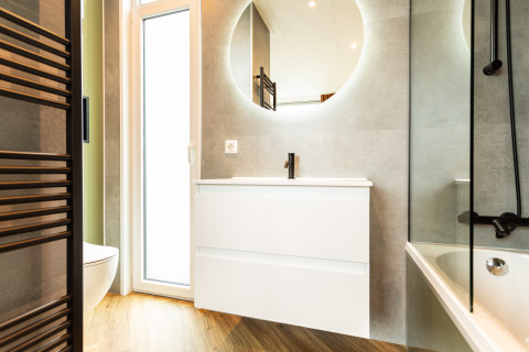 Baño moderno en Waterhoeve Wellness (Hottub), Park Westerkogge, Países Bajos, con espejo circular iluminado.
