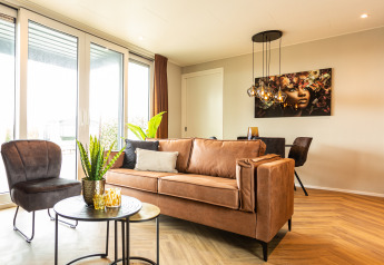 Salon moderne avec grandes fenêtres, canapé en cuir et œuvre d'art murale à Waterhoeve Wellness, Park Westerkogge.