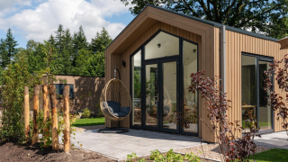 Modern Tiny Lodge with wooden exterior, large glass doors, and hanging chair on sunny patio outside.