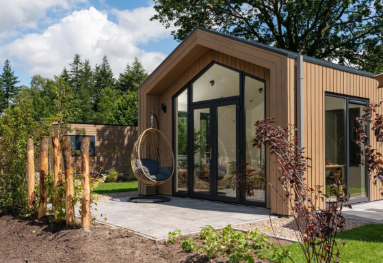 Modern Tiny Lodge with wooden exterior, large glass doors, and hanging chair on sunny patio outside.
