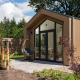Moderne Tiny Lodge med glasdør, træbeklædning og hængestol på terrassen, omgivet af natur.