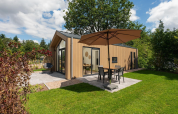 Lille lodge med boblebad, parasol og terrasse på Veluwepark de Bosgraaf, Holland, omgivet af natur.