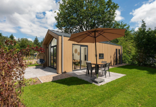 Modern tiny lodge with hot tub, large patio umbrella and outdoor seating at Veluwepark de Bosgraaf, NL.