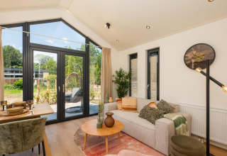 Modern living area in Tiny Lodge at Veluwepark de Bosgraaf, with large windows, sofa, and nature view.