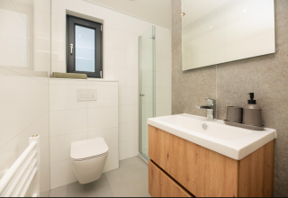 Modern bathroom at Tiny Lodge featuring wooden sink unit, wall-mounted toilet, and glass shower at Veluwepark de Bosgraaf.