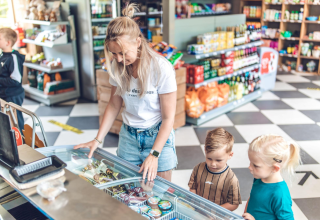 A mother and two children select ice cream from a freezer in a shop at Tiny Lodge with hot tub at Veluwepark de Bosgraaf.