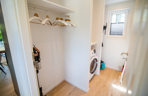 Waschküche in der Forest Lodge Comfort im Bospark Markelo, Niederlande, mit Waschmaschine und Kleiderbügeln.