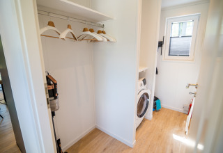 Waschküche in der Forest Lodge Comfort im Bospark Markelo, Niederlande, mit Waschmaschine und Kleiderbügeln.