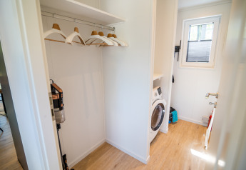 Waschküche in der Forest Lodge Comfort im Bospark Markelo, Niederlande, mit Waschmaschine und Kleiderbügeln.