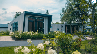 Modern lodge called Just Nature, surrounded by green plants and flowers in a peaceful, natural setting.