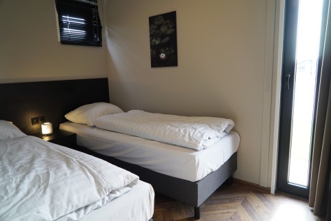 Cozy lodge room with two single beds, a bedside lamp, wall art, and natural light coming through a window.