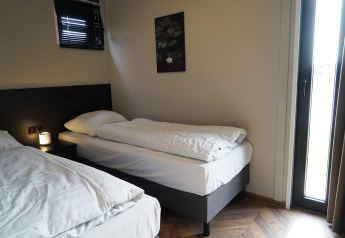 Knusse lodgekamer met twee eenpersoonsbedden, een nachtlampje, muurkunst en natuurlijk licht door het raam.