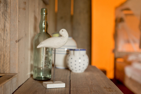 Houten vogel, glazen fles en potten op een rustieke plank in een safaritent bij Club Les Ormes, Frankrijk.