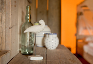 Houten vogel, glazen fles en potten op een rustieke plank in een safaritent bij Club Les Ormes, Frankrijk.