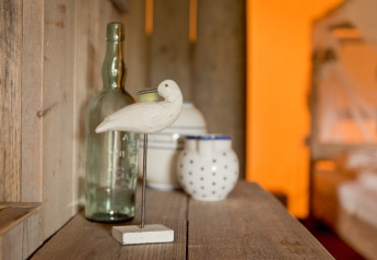 Houten vogel, glazen fles en potten op een rustieke plank in een safaritent bij Club Les Ormes, Frankrijk.
