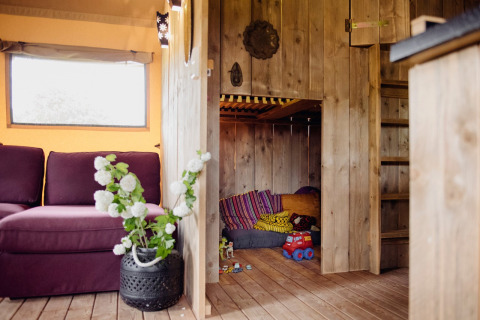 Cozy play nook with wooden walls and colorful cushions in a safari tent at Club Les Ormes, France.