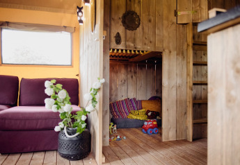 Cozy play nook with wooden walls and colorful cushions in a safari tent at Club Les Ormes, France.