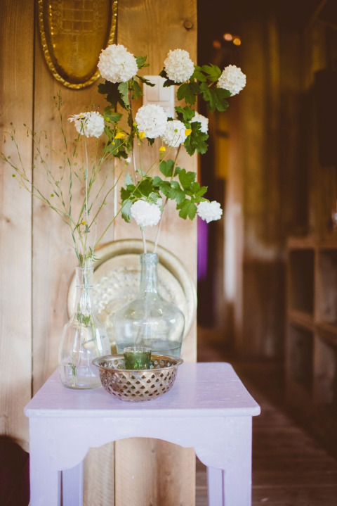 Klein tafeltje met glazen vazen met witte bloemen en metalen schaaltje in safaritent bij Club Les Ormes, Frankrijk.