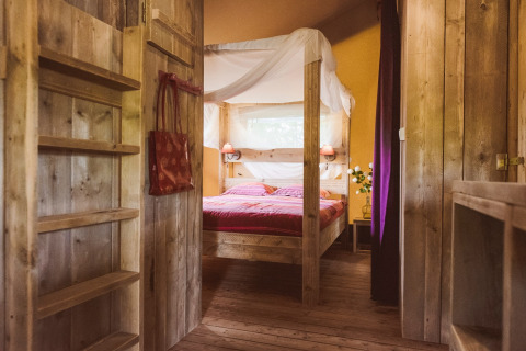 Interno di tenda safari al Club Les Ormes, Francia, con letto a baldacchino e arredamento rustico in legno.