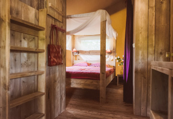 Interno di tenda safari al Club Les Ormes, Francia, con letto a baldacchino e arredamento rustico in legno.