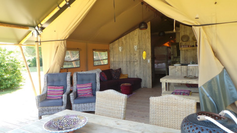 Interior of a safari tent with wicker furniture and wooden walls at Club Les Ormes in France.