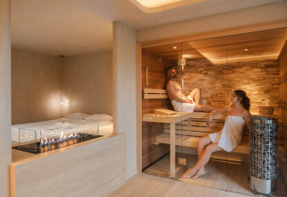 Suite de bienestar en Woodz Lodges, Bélgica, con dos personas en sauna y una moderna chimenea interior.