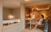 Wellness Suite at Woodz Lodges, Belgium, featuring two people in a sauna and a stylish indoor fireplace.