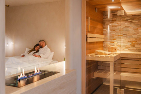 Pareja relajándose en una suite wellness con chimenea moderna y sauna en Woodz Lodges, Bélgica.