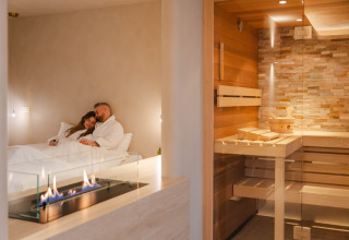 Pareja relajándose en una suite wellness con chimenea moderna y sauna en Woodz Lodges, Bélgica.