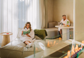 Two people relax in the Wellness Suite at Woodz Lodges in Belgium, both wearing white robes indoors.