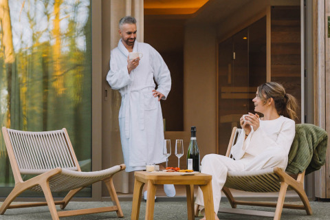 Pareja disfruta de bebidas en la terraza de la Wellness Suite en Woodz Lodges, Bélgica, ambiente relajado.