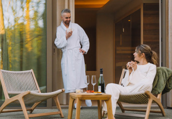 Pareja disfruta de bebidas en la terraza de la Wellness Suite en Woodz Lodges, Bélgica, ambiente relajado.