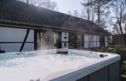 Udendørs jacuzzi med bobler og damp foran en traditionel lodge, Villa Lodge, hos Woodz Lodges i Belgien.