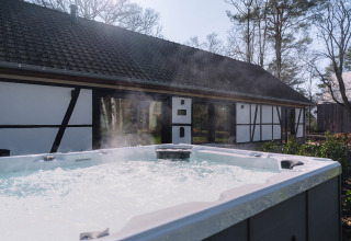 Buitenjacuzzi met damp tegenover Villa Lodge bij Woodz Lodges in België, omringd door groen.
