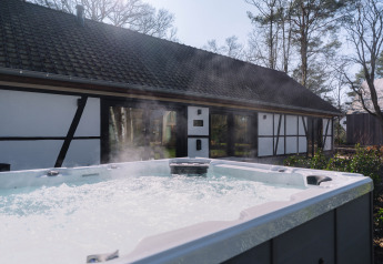Udendørs jacuzzi med bobler og damp foran en traditionel lodge, Villa Lodge, hos Woodz Lodges i Belgien.