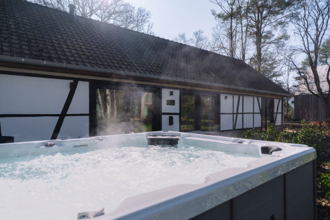 Udendørs jacuzzi med bobler og damp foran en traditionel lodge, Villa Lodge, hos Woodz Lodges i Belgien.
