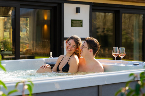 Pareja relajándose en jacuzzi con dos copas de vino en Villa Lodge en Woodz Lodges, Bélgica.