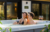 Koppel ontspant in de jacuzzi met twee glazen wijn bij Villa Lodge op Woodz Lodges in België.