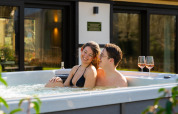 Koppel ontspant in de jacuzzi met twee glazen wijn bij Villa Lodge op Woodz Lodges in België.
