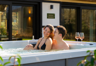 Coppia che si rilassa in jacuzzi con due bicchieri di vino presso Villa Lodge, Woodz Lodges in Belgio.