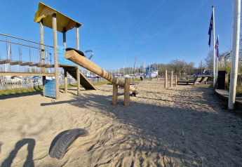 Playground with seesaw, slide, and rope bridge on sand at a glamping accommodation on a sunny day.