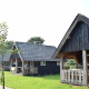 Cabañas de madera en Wood Lodge, con porches y techos de tejas, rodeadas de césped verde y árboles.