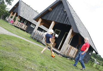 Enfant et adulte jouent au foot devant des chalets noirs au Wood Lodge, Holiday park De Boshoek, Pays-Bas.